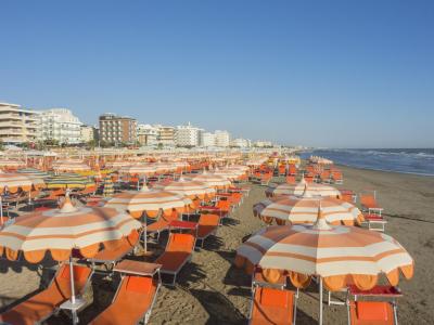 Spiaggia affollata con ombrelloni arancioni e edifici sullo sfondo.