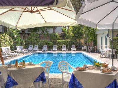 Piscina all'aperto con sedie a sdraio e tavoli apparecchiati per colazione.