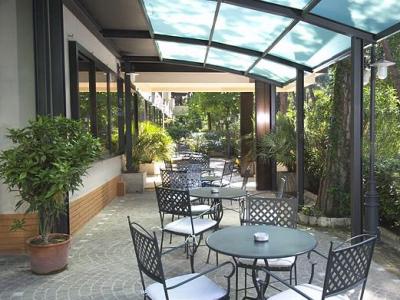 Terrazza coperta con tavoli e sedie, circondata da verde lussureggiante.