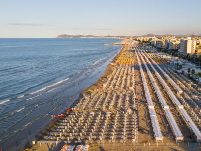 Spiaggia affollata con ombrelloni e mare calmo, città sullo sfondo.