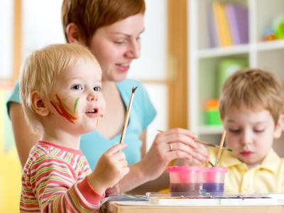 Bambini e adulto dipingono insieme, volti colorati e felici.