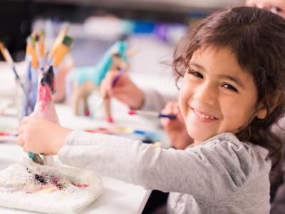 Bambina sorridente dipinge un cavallo con colori vivaci.