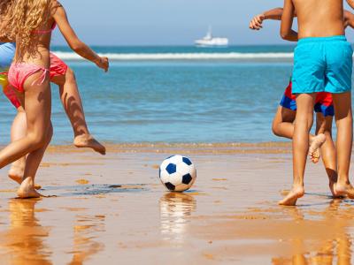 Bambini giocano a calcio sulla spiaggia, giornata soleggiata.