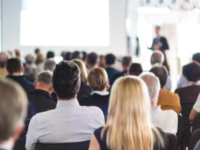 Persone sedute ascoltano una presentazione in una sala conferenze.