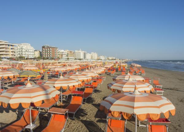 Spiaggia affollata con ombrelloni arancioni e edifici sullo sfondo.