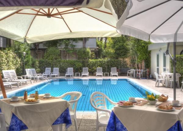 Piscina all'aperto con sedie a sdraio e tavoli apparecchiati per colazione.