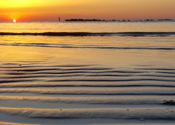 Tramonto sul mare con riflessi dorati e onde leggere.