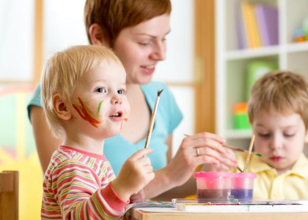 Bambini e adulto dipingono insieme, volti colorati e felici.