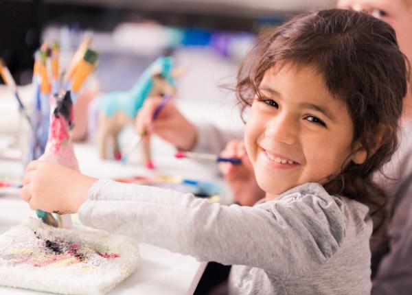 Bambina sorridente dipinge un cavallo con colori vivaci.