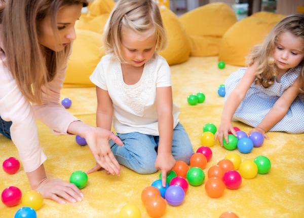 Bambini giocano con palline colorate su un tappeto giallo.