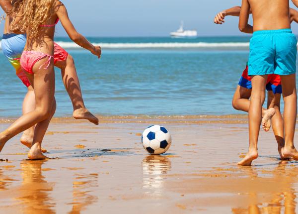 Bambini giocano a calcio sulla spiaggia, giornata soleggiata.