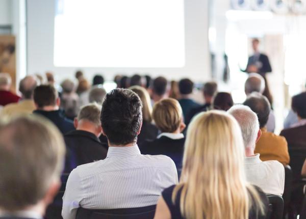 Persone sedute ascoltano una presentazione in una sala conferenze.